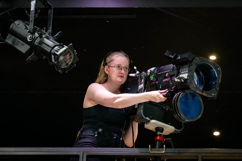 A woman studying technical theatre at Mountview, pointing a stage light. 