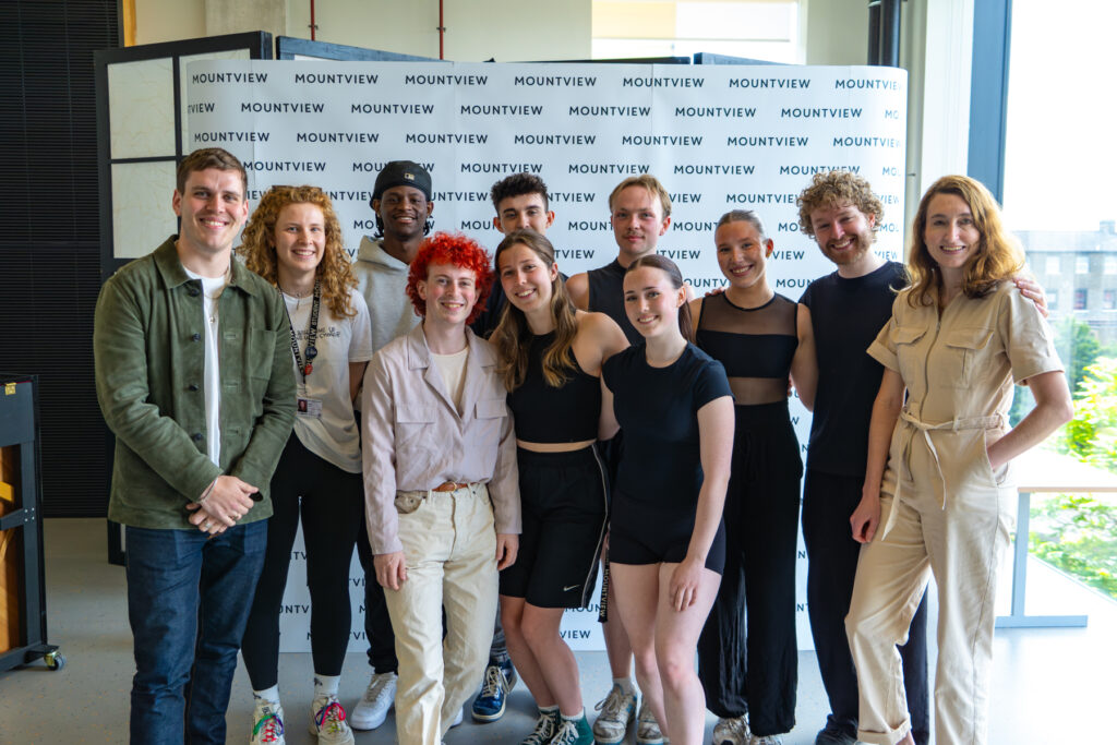 A photograph of Crossroads Live staff and scholars smiling in bright studio against a step and repeat Mountview banner.